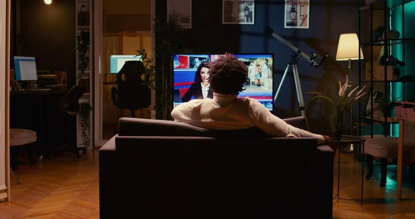 Человек использует ультраширокий смарт‑телевизор в гостиной с неоновым освещением, чтобы развлечься после работы.